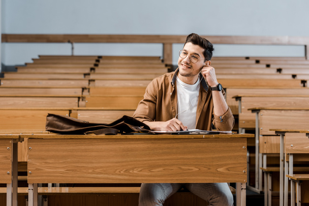 Улыбающийся студент в очках сидит за столом и смотрит в сторону в классе
 - Фото, изображение