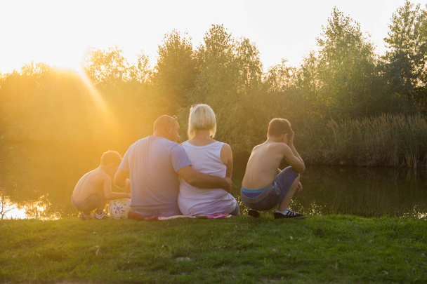 Onnellinen perhe istuu järven rannalla ja katselee auringonlaskua
 - Valokuva, kuva