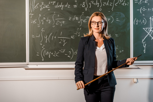 приваблива вчителька-жіночка з дерев'яним вказівником, що пояснює математичні рівняння в класі
 - Фото, зображення