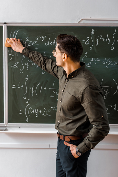 male teacher wiping mathematical equations with sponge from chalkboard in classroom - Фото, зображення