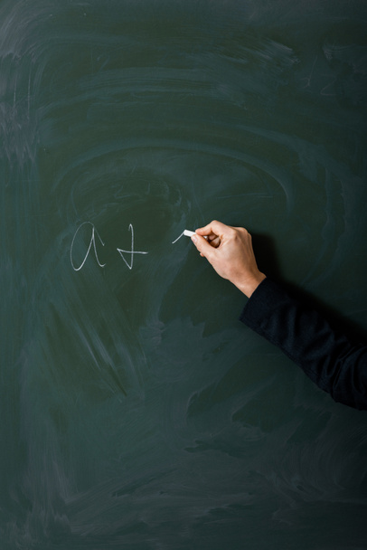 partial view of female teacher writing equation on green chalkboard - Photo, Image