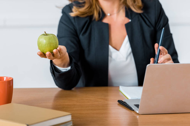 vista ritagliata dell'insegnante seduto alla scrivania del computer e con mela in mano
 - Foto, immagini