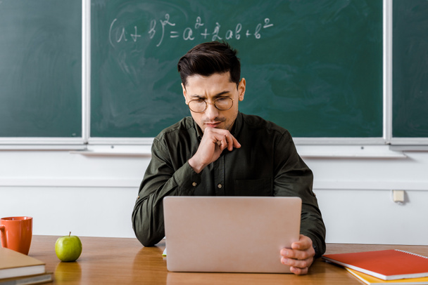 insegnante maschio pensieroso in occhiali seduto alla scrivania e utilizzando il computer in classe
 - Foto, immagini