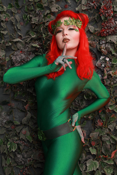 όμορφη νεαρή γυναίκα με τα κόκκινα μαλλιά θέτοντας σε πράσινο κοστούμι κοντά τα φύλλα - Φωτογραφία, εικόνα