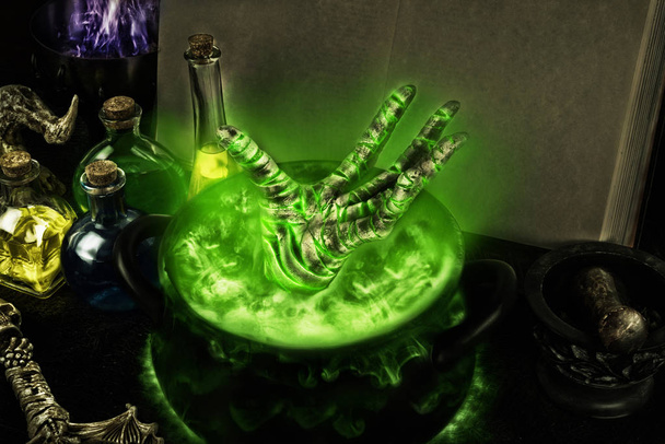 Halloween composition of boiling cauldron, mysterious bottles and black magic book. - Photo, Image
