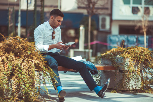 Un uomo bello elegante è seduto sulla panchina nel centro della città e guardando interessato al suo tablet
 - Foto, immagini