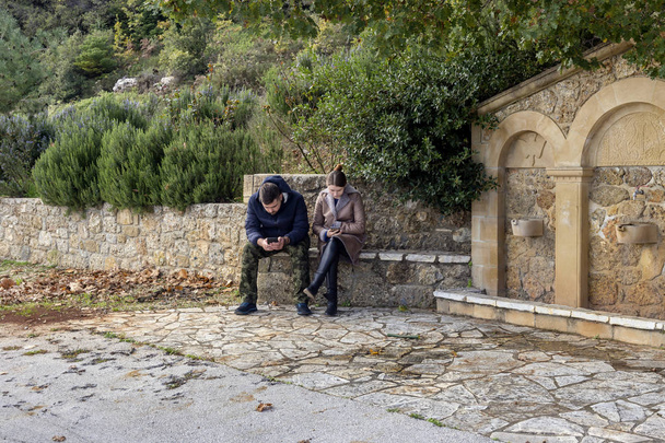 Le concept de solitude ensemble. Un jeune couple est assis sur un banc près du parc et chacun d'eux regarde dans son téléphone
. - Photo, image