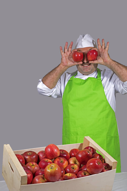Vendedor de frutas bromeando con dos manzanas rojas sobre sus ojos
. - Foto, Imagen
