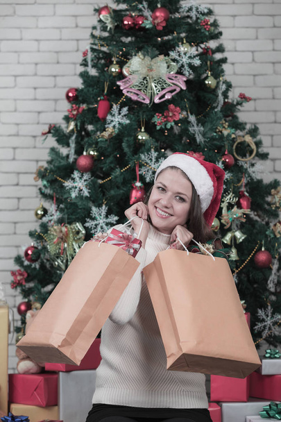 Young and beautiful caucasian woman in red hat and holding bag of gift boxes look at the camera clouse up shot.Concept for good time in christmas festival. - Foto, Imagen