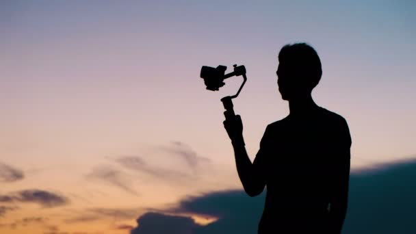 Silhouetten van een toeristische man met een stabilisator en een videocamera close-up - Video