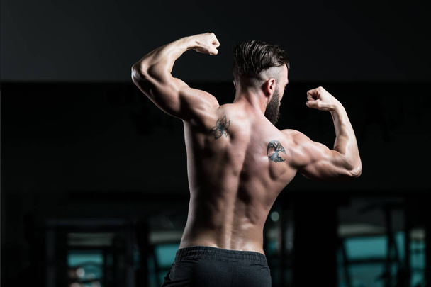 Beau jeune homme debout fort dans le gymnase et les muscles flexibles - Bodybuilder athlétique musculaire Fitness Model Poser après des exercices - Photo, image