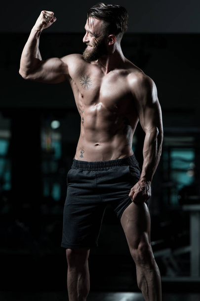 Handsome Young Man Standing Strong In The Gym And Flexing Muscles - Muscular Athletic Bodybuilder Fitness Model Posing After Exercises - Fotó, kép