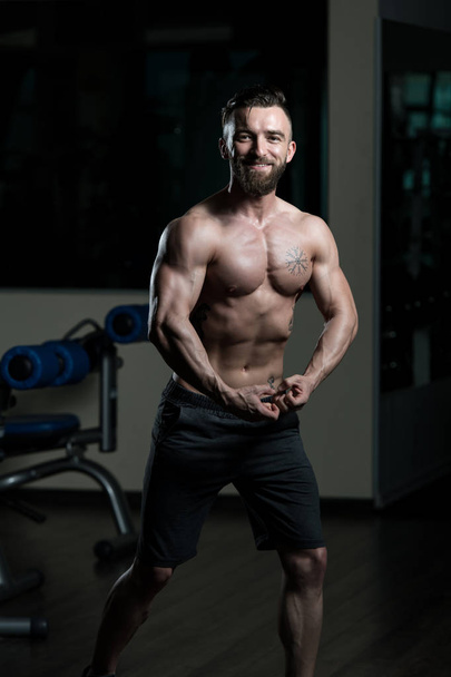 Young Man Standing Strong In The Gym And Flexing Muscles - Muscular Athletic Bodybuilder Fitness Model Posing After Exercises - Fotó, kép