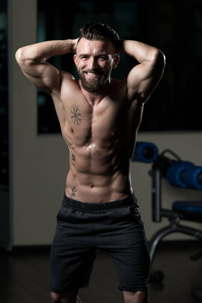 Przystojny Młody Człowiek Stojący Silny W Siłowni i Flexing Muscles - Muscular Athletic Bodybuilder Fitness Model Pozowanie Po Ćwiczeniach - Zdjęcie, obraz