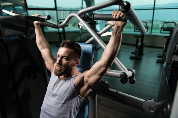 Man In The Gym Exercising On His Shoulders On Machine With Cable In The Gym - Photo, image