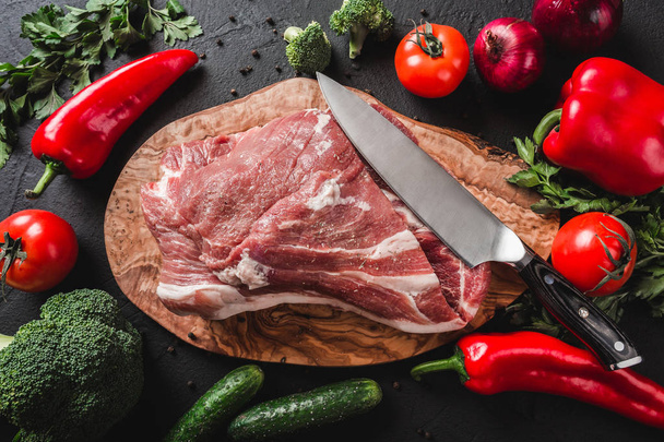 Carne cruda, filete de res en tabla de cortar con cuchillo sobre fondo negro con ingredientes para cocinar. Vista superior
 - Foto, imagen