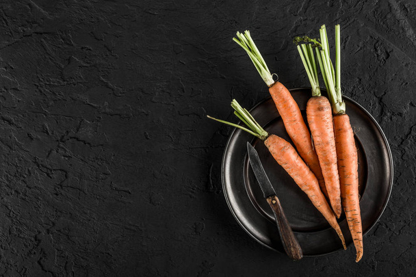 Fresh carrots bunch on a plate over dark stone background. Food concept, top view, copy space - Fotografie, Obrázek