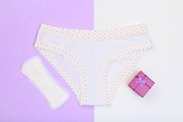 Beautiful panties with sanitary napkin and gift box on lilac and white background. Women underwear set. Romantic lingerie. Top view. - Фото, зображення