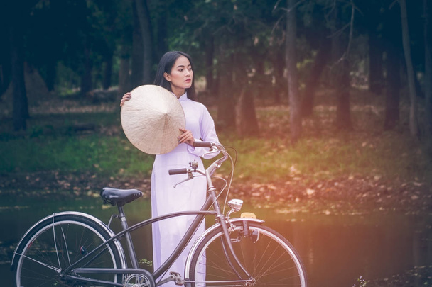 Портрет красива молода Азіатського підлітка з довгим волоссям, носити костюм В'єтнаму (АО dai) вона в даний час відбуксирували велосипед і проведення капелюх тлі зелені сади з копією простір. - Фото, зображення