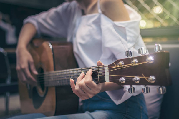 Asian girls wearing white shirts and jeans. She is sitting on a black couch is currently vacationing by playing guitar in a coffee shop. - 写真・画像