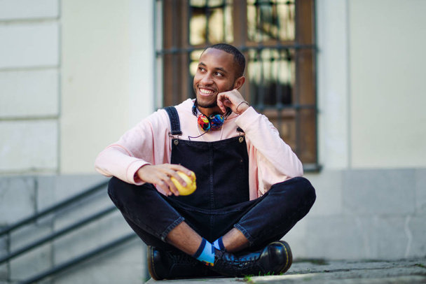 都市の手順の上に座ってリンゴを食べる若い黒人男性。ライフ スタイルのコンセプト. - 写真・画像