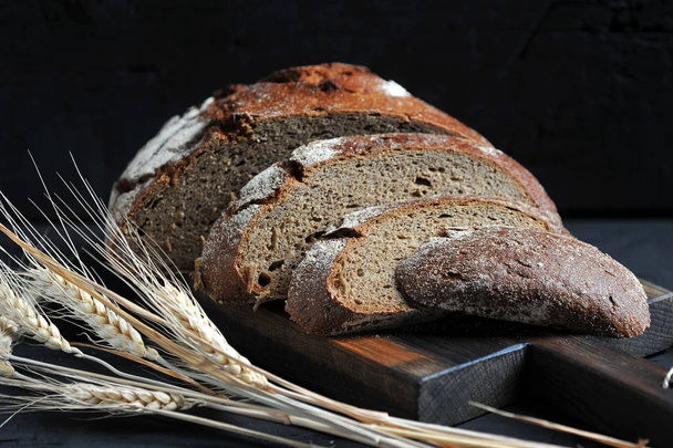 rye bread, cut into pieces and ears on dark rustic background - Fotografie, Obrázek