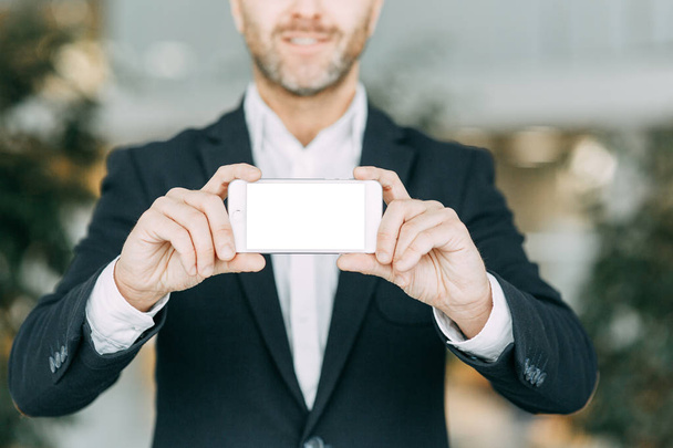 The phone in the hand of a business man, with a white screen. Blank for designers with bokeh. - Foto, imagen
