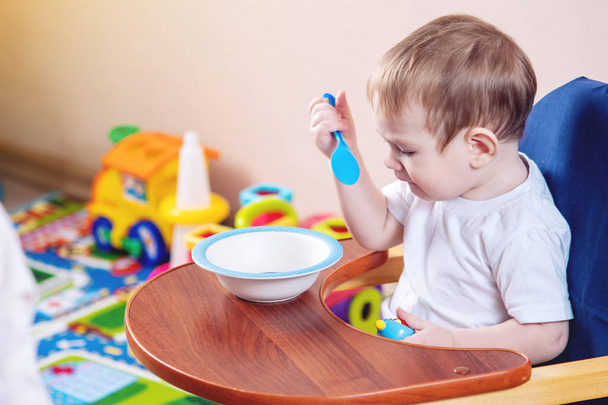 Malý chlapeček, naučit se jíst u stolu velké dítě studuje na talíř a lžící v kuchyni - Fotografie, Obrázek
