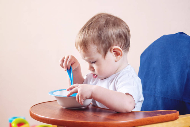 プレートと台所でスプーンを勉強して子供のテーブルで食事をする学習の小さなかわいい男の子 - 写真・画像