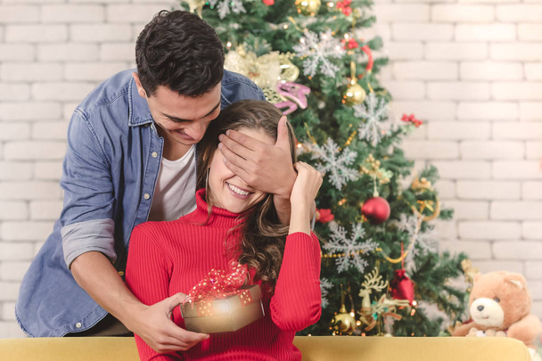 Young and handsome caucasian man standing behide beautiful woman and close her eyes and give her gift box. Concept for good moment and sharing best time in christmas festival. - Photo, Image