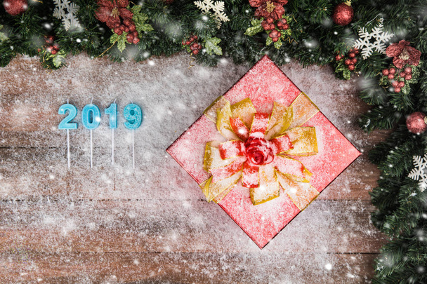 Одна ошеломляющая красная подарочная коробка золотая лента, сосновые ветви и красная граница ягод. Копировать пространство слева с деревянной доской и расплывчатой снежинкой, включая синий цвет 2019 года
. - Фото, изображение