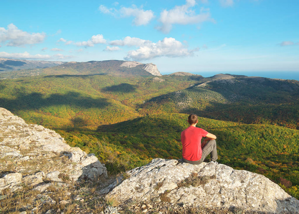 Man sitting on the edge of cliff mountain. Conceptual scene. - Фото, изображение