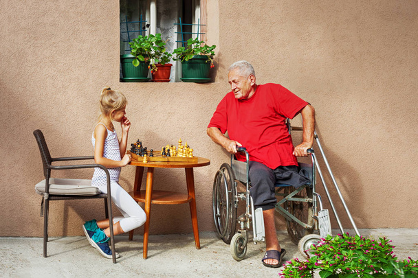 Disabled Senior and his beautiful young granddaughter playing chess and smiling outside - Фото, зображення