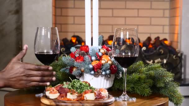 Feestdagen en Nieuwjaar viering concept. Close-up van handen van een Afro-Amerikaans nemen een glas met rode wijn met Kerstmis. Gezellige haard op de achtergrond. 4k - Video