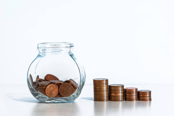Монеты в стеклянной банке и стопки монет на белом фоне
 - Фото, изображение