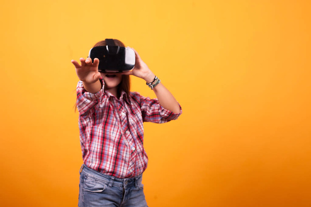 Маленькая девочка валяет дурака со своим VR на жёлтом фоне в студии
 - Фото, изображение