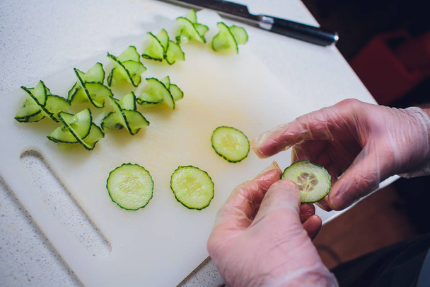 Cooks hands cutting fresh cucumber on wooden board - Photo, image