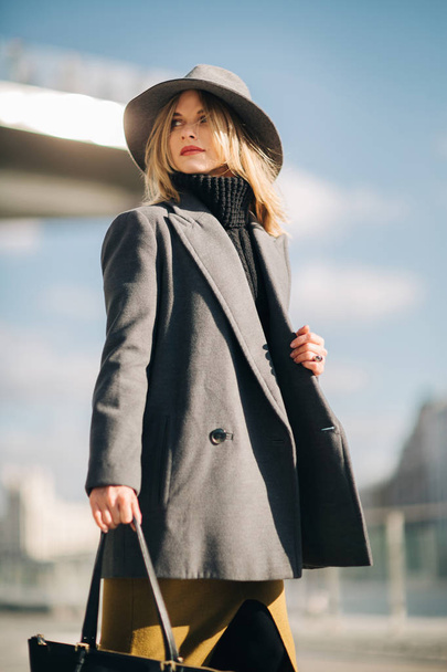 Photo below of young blonde in gray coat and hat against blue sky and building - Foto, Bild