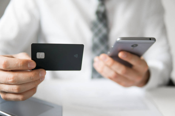 Online payments through the phone. Young businessman with a bank credit card in his hands. Payment of goods online. Online trading on the currency exchange. Smartphone and Internet Commerce. - Foto, Bild