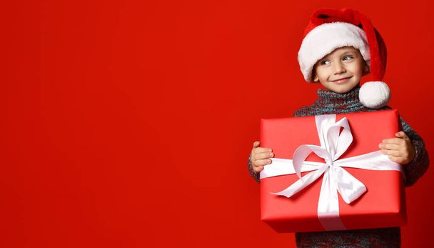 Smiling funny child in Santa red hat holding Christmas gift in hand. Christmas concept. - Foto, Bild
