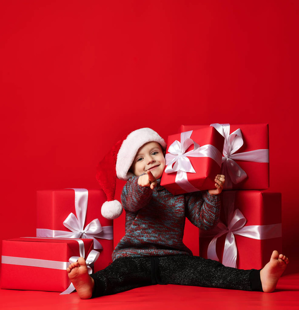 Smiling funny child in Santa red hat holding Christmas gift in hand. Christmas concept. - Fotó, kép
