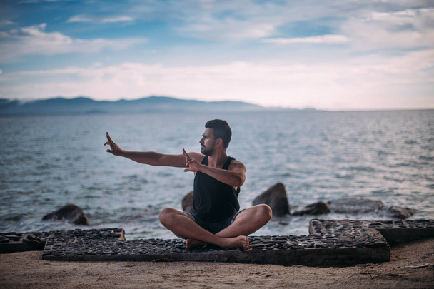 Young man doing yoga by the sea. A handsome guy is sitting on the ocean at sunset. - Foto, Bild