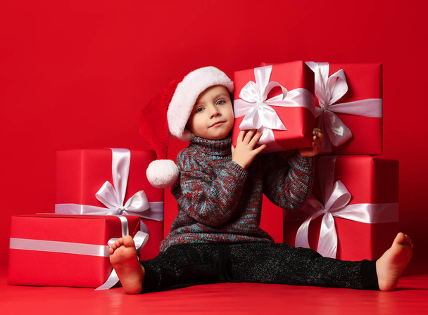 Smiling funny child in Santa red hat holding Christmas gift in hand. Christmas concept. - Foto, Imagem