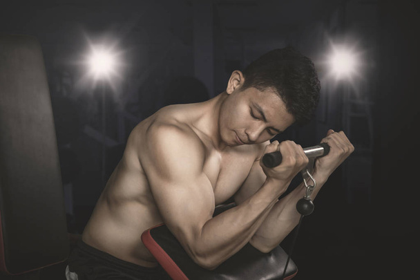 Image of muscular man doing exercise with a weight machine in dark background - 写真・画像