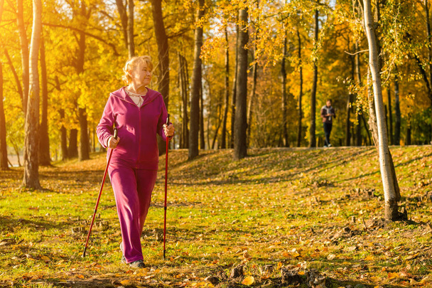 Active senior woman hiking walks at colorful Sunny autumn park. Healthy lifestyle. Finland. - Photo, Image