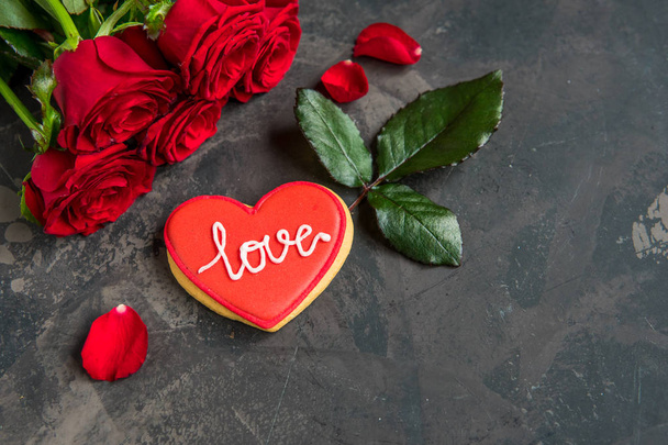 Červené růže a cookie ve tvaru srdce s textem lásku, tmavé pozadí kopie prostor. - Fotografie, Obrázek
