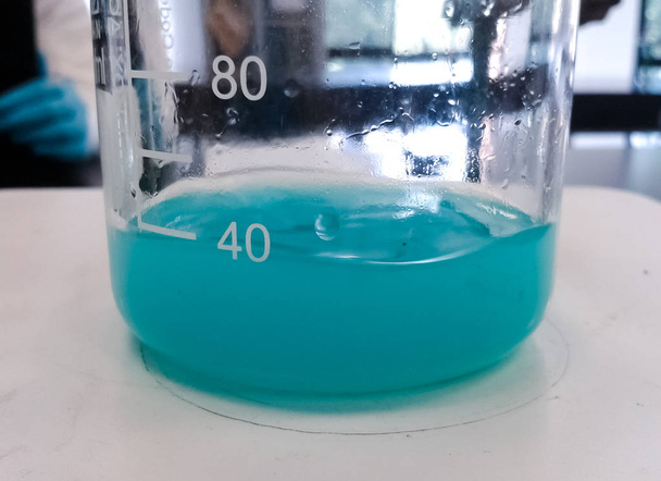 Kemiallinen reaktio, jossa turkoosi tai akvamariini nestemäinen aine on lasidekantterissa. Tieteellinen laboratoriotausta
. - Valokuva, kuva