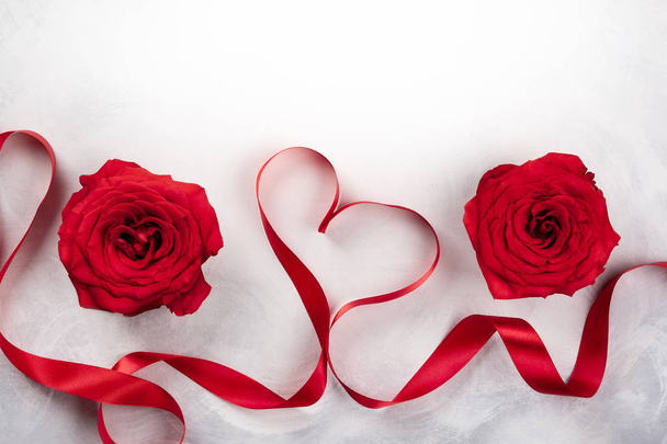 Red roses and red ribbon in shape of heart on the vintage white-grey background. Festive concept for Valentines day. Top view with copy space. - Photo, image
