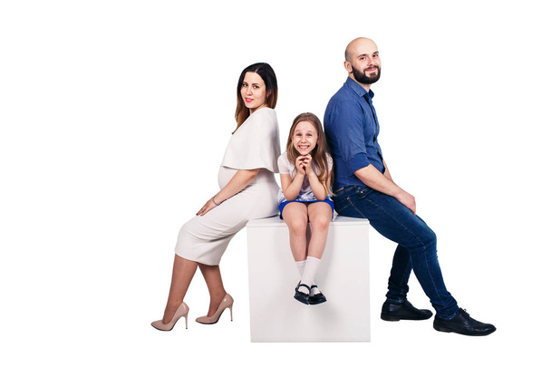 glückliche junge Familie sitzt auf einem Sockel vor weißem Hintergrund. - Foto, Bild