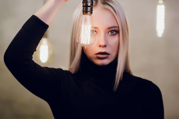 Beautiful girl in black body, bathing suit on a dark background with light bulbs. A girl with red lipstick posing in front of the camera. Girl of athletic appearance is sitting on a bar stool. - Valokuva, kuva